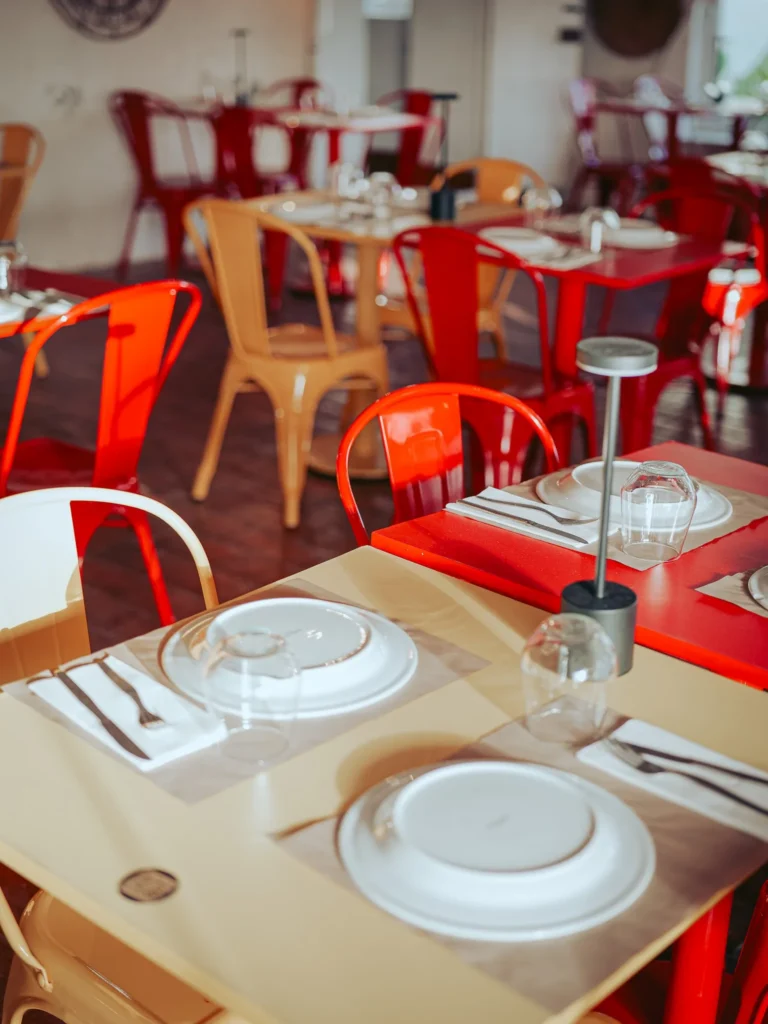 Tables set in the colorful dining room of the Lumo restaurant in Tavira, with red and yellow chairs and a bright atmosphere during the day.