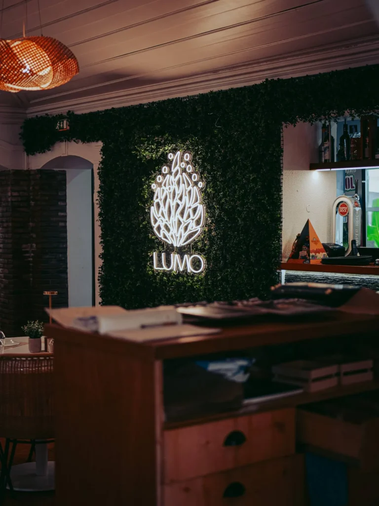 Interior of the Lumo restaurant in Tavira with a green wall and a glowing logo, warm atmosphere and wooden furniture.