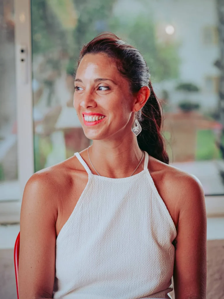 Caroline sitting inside the Lumo restaurant in Tavira, smiling in front of a large window with a view of a summer garden.
