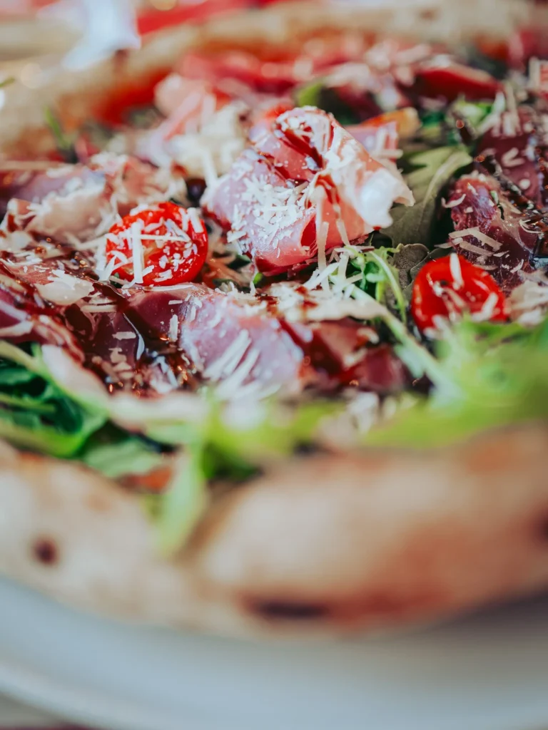 Close-up of a pizza topped with Parma ham, arugula, cherry tomatoes, cheese shavings, and balsamic reduction, served in a restaurant in Tavira, Algarve.
