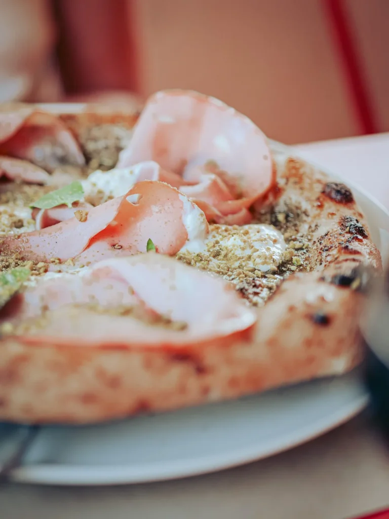 Close-up of a pizza topped with mortadella, pesto, pistachio, and stracciatella, served on a plate at Lumo restaurant in Tavira, Algarve.
