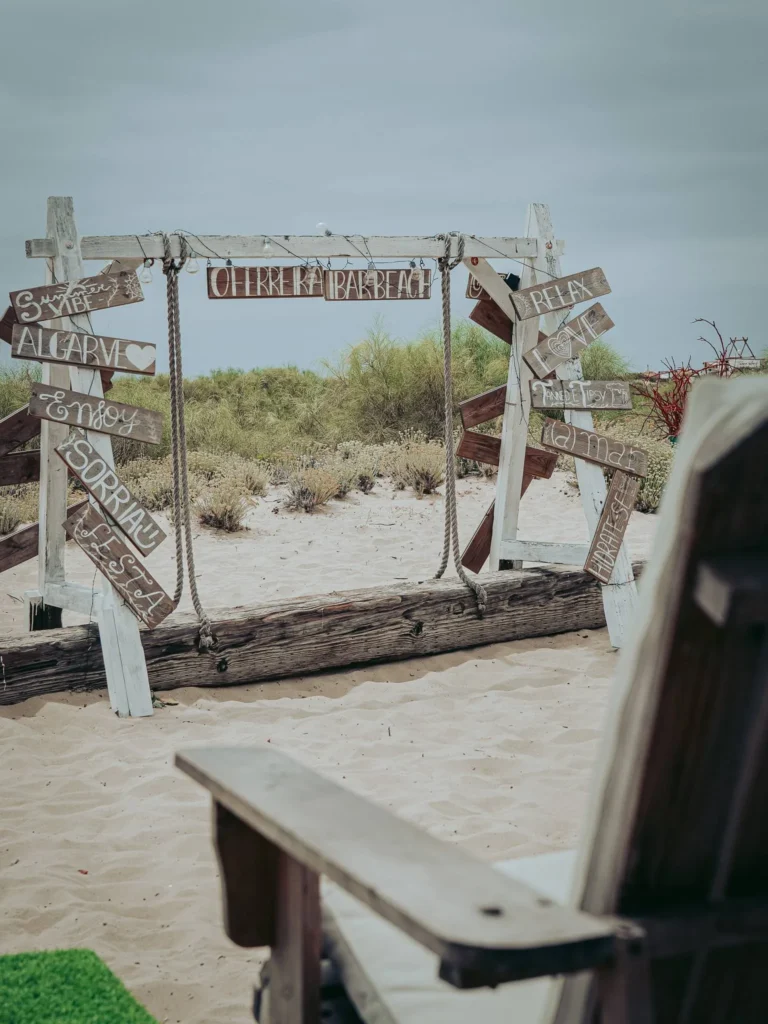 Entrance to a landscaped beach with decorative wooden panels on the sand of Tavira Island, Algarve, under a cloudy sky.