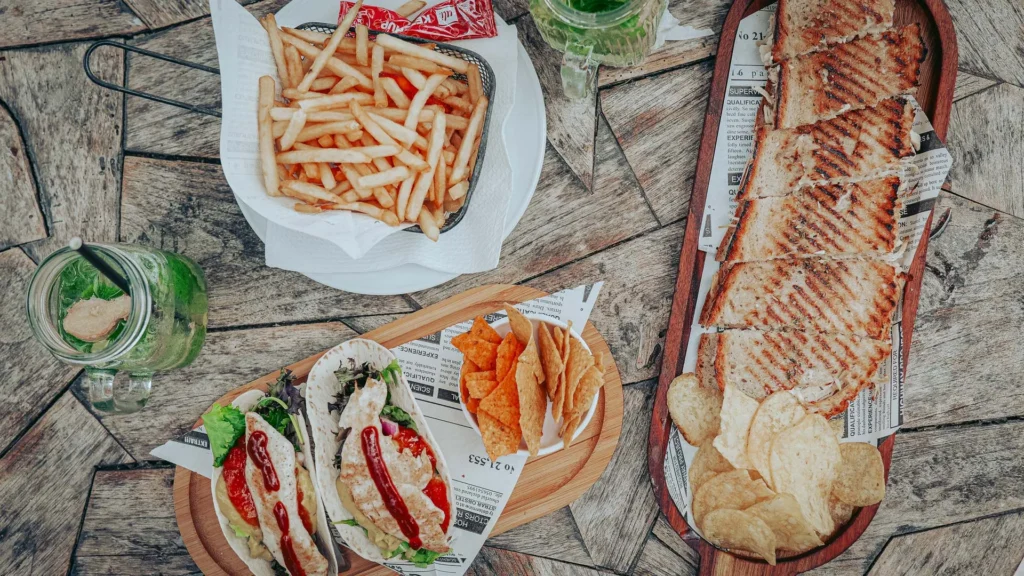 Assortment of chicken tosta, chicken tacos, fries, chips, and ginger mint lemonade on a wooden table at O Ferreira, Tavira Island, Algarve, Portugal, in June 2026. No visible diners.