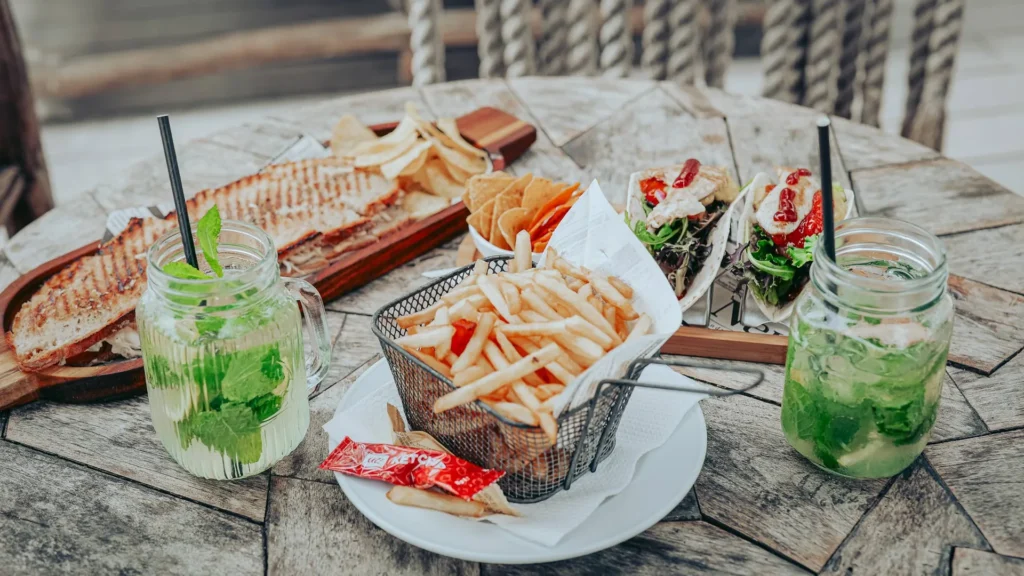 Meal consisting of a chicken tosta, chicken tacos, fries, and ginger and mint lemonades on a wooden table outside, probably on Tavira Island in the Algarve, Portugal in June.