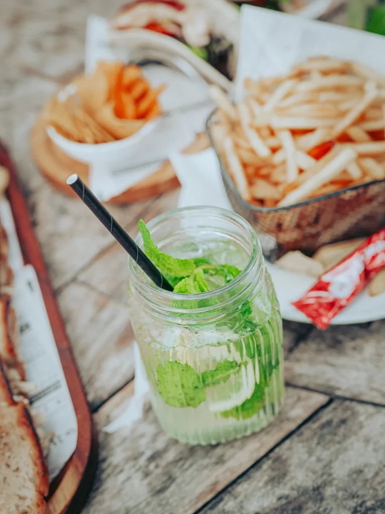 A glass of ginger and mint lemonade is placed on a wooden table, accompanied by fries and chicken tacos in a summery setting at Tavira Island, Algarve.