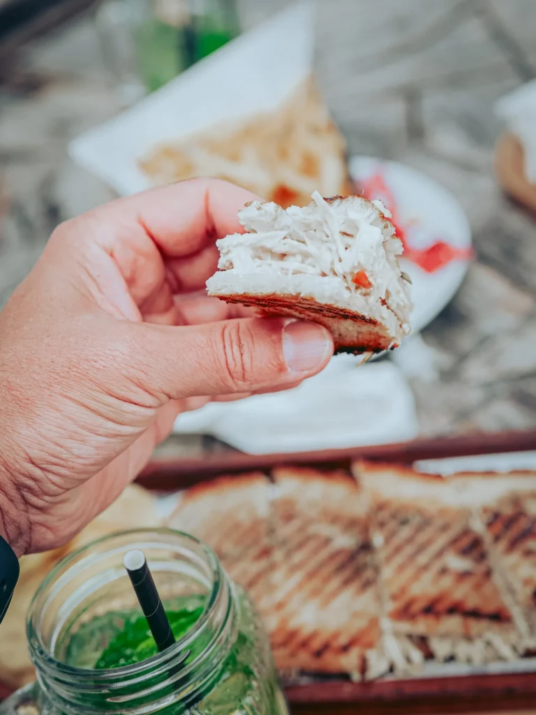 Hand-held chicken tosta on a wooden table, with a ginger and mint lemonade in a jar in the foreground.