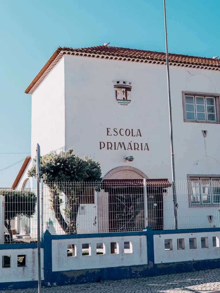 Facade of a primary school in Porto Covo, typical white building of Alentejo under a blue sky, with no visible human presence.
