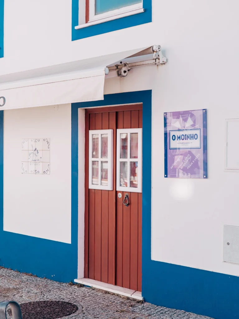 Facade of a typical Porto Covo building with a wooden door, blue framing, and a sign 'O Moinho'.