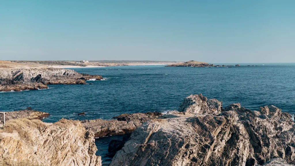 Rocky coast of Porto Covo in Alentejo, Portugal, overlooking the Atlantic Ocean under a clear sky in June.