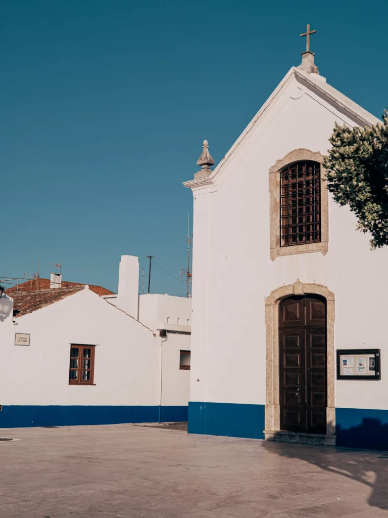 Facade of a small white church with a blue base under a clear sky in Porto Covo, in the Alentejo region of Portugal, in June.