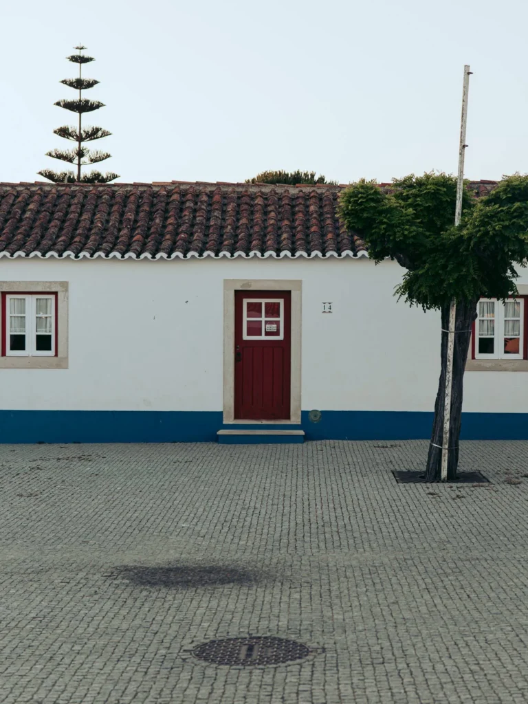 Traditional white house with red shutters and tiled roof, typical of Porto Covo in Alentejo, Portugal, photographed in June 2026.