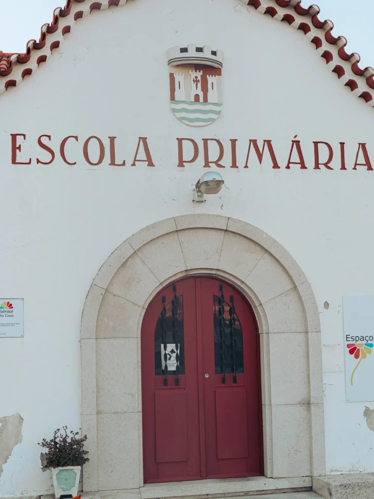 Facade of a primary school in Porto Covo, in Alentejo, Portugal, with a red door and a coat of arms above the entrance.