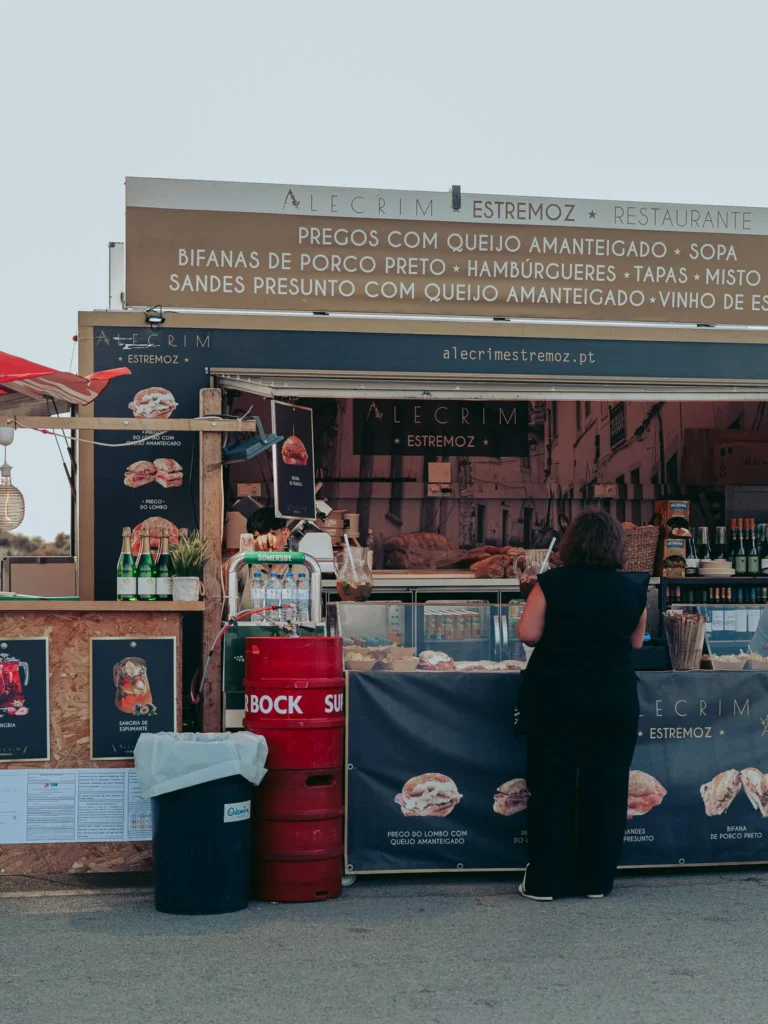 Alecrim Estremoz food stand offering presunto com queijo amanteigado sandwiches at the Fai-Tur Festival in Vila Nova de Milfontes, summer outdoor atmosphere.