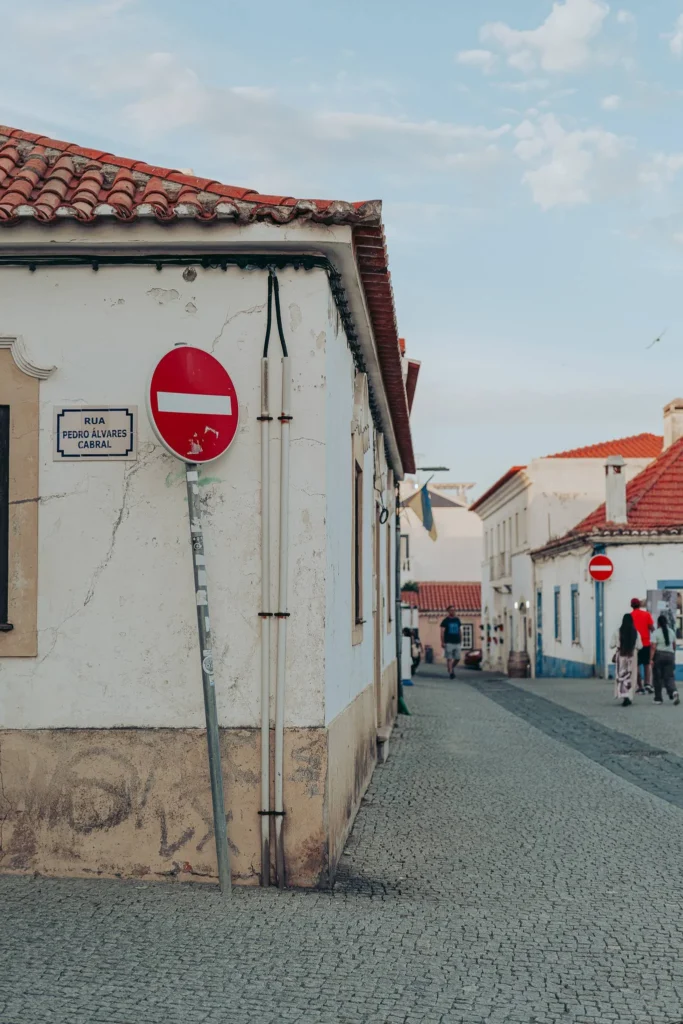 Paved street in the center of Vila Nova de Milfontes with traditional houses featuring red roofs and a no entry sign, at the end of the day.