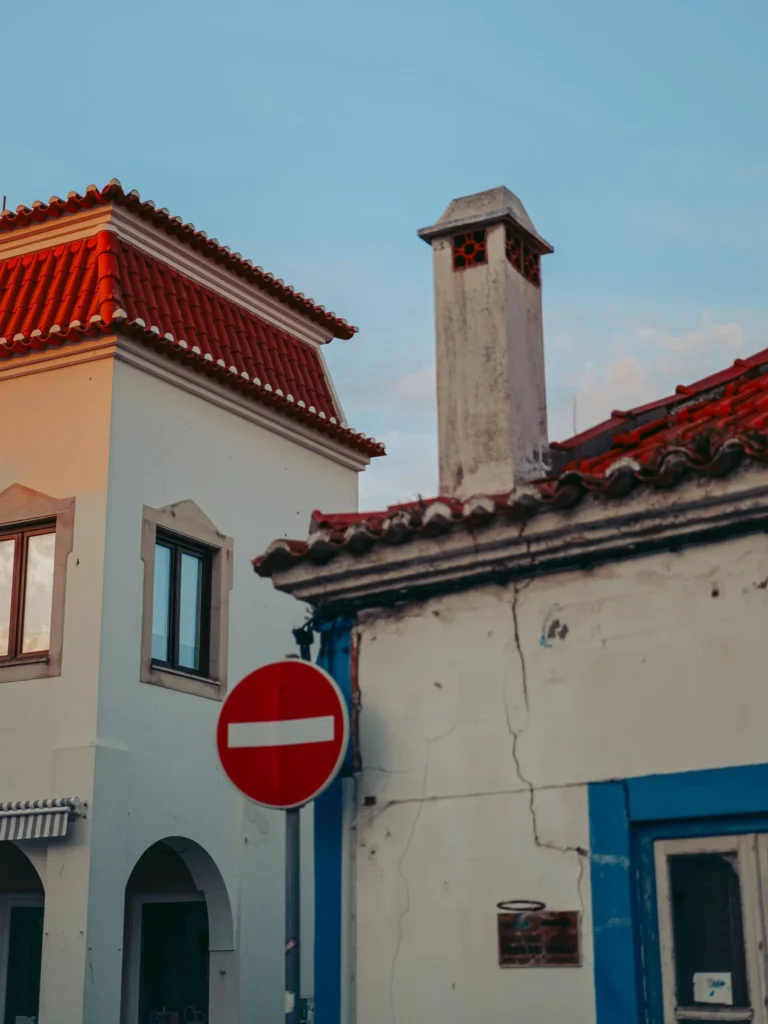Traditional houses with red roofs and a no entry sign on a street in Vila Nova de Milfontes, Alentejo, under a clear sky.