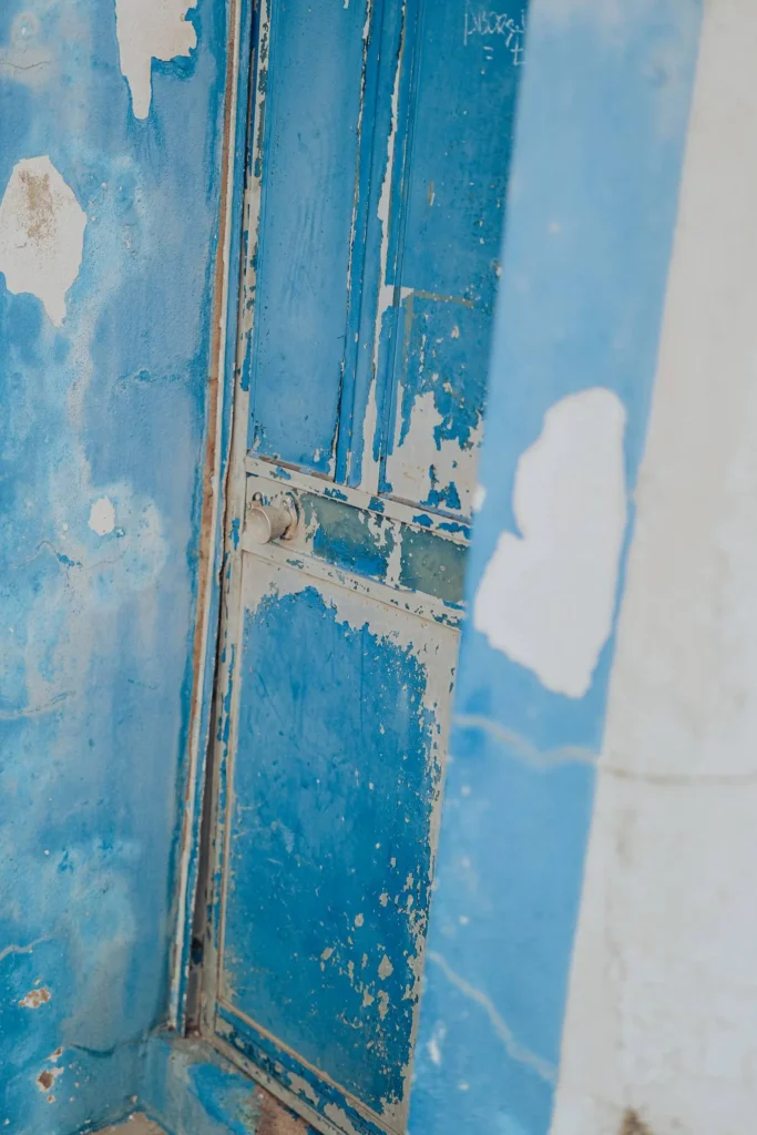 Old blue chipped wooden door on a wall also painted in blue and white, typical of traditional Portuguese architecture in Vila Nova de Milfontes in Alentejo.