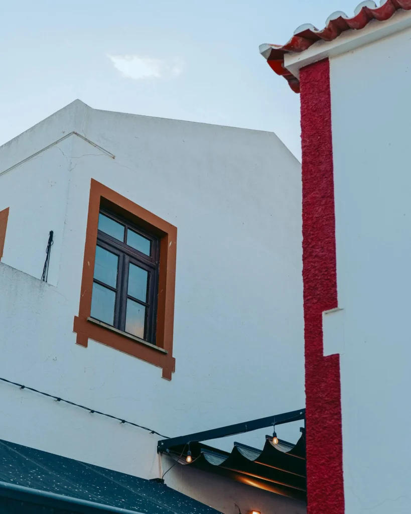 White house facade with ochre window frames and a red wall, typical of Portuguese architecture in Vila Nova de Milfontes in Alentejo.