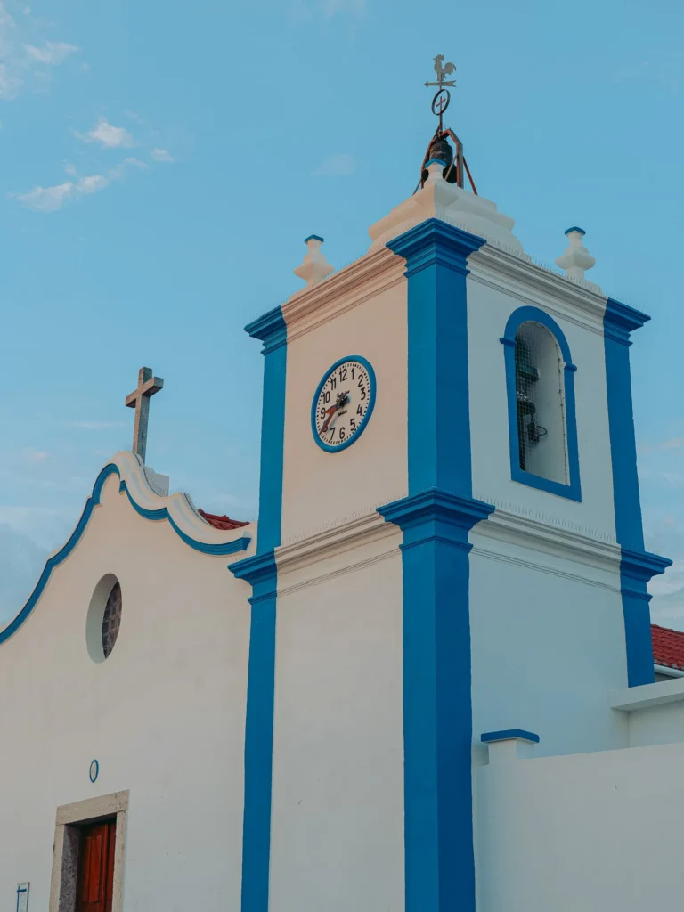 Facade of a white church with blue outlines in Vila Nova de Milfontes, typical of Alentejo in Portugal, under a clear sky in June.