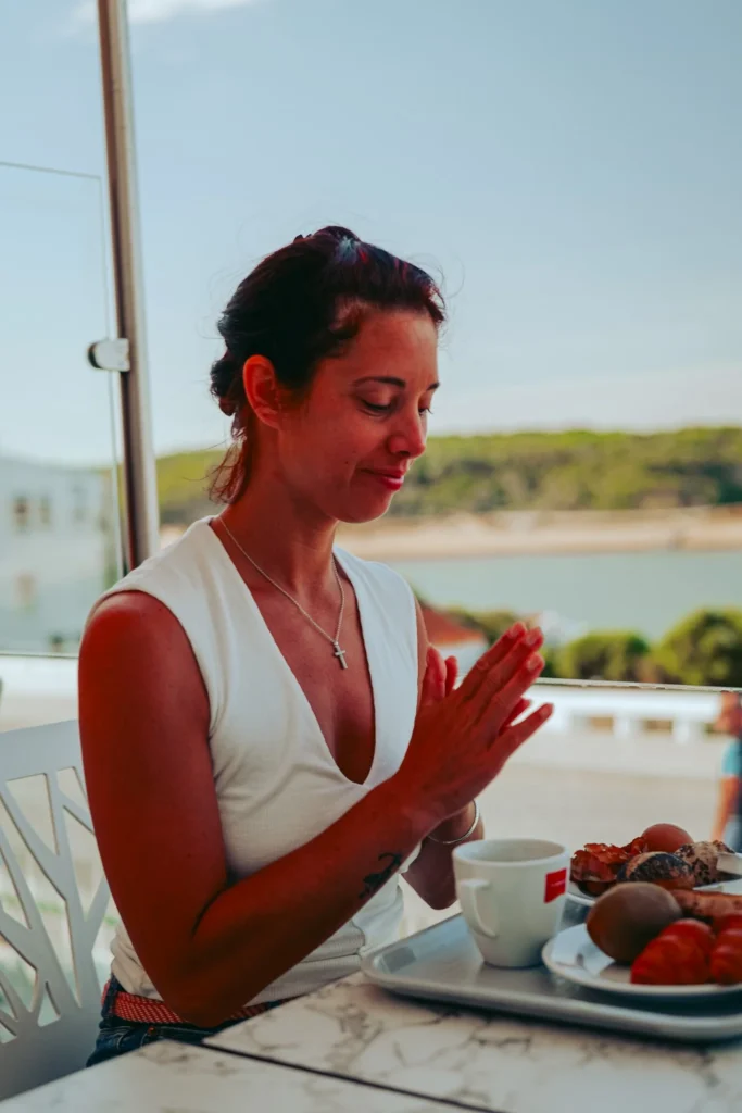 Caroline sitting on the terrace at Duna Parque Hotel in Vila Nova de Milfontes, having breakfast with a view of nature in the background.
