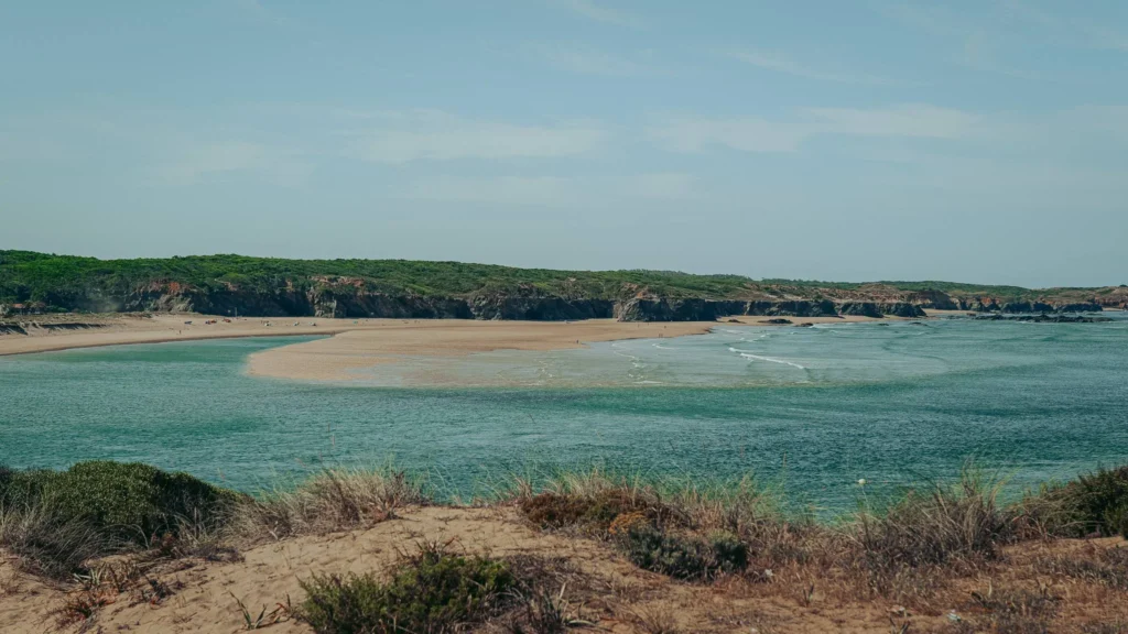 Wild beach with sandy banks and turquoise water in Vila Nova de Milfontes, in Alentejo, Portugal, under a clear sky in June.