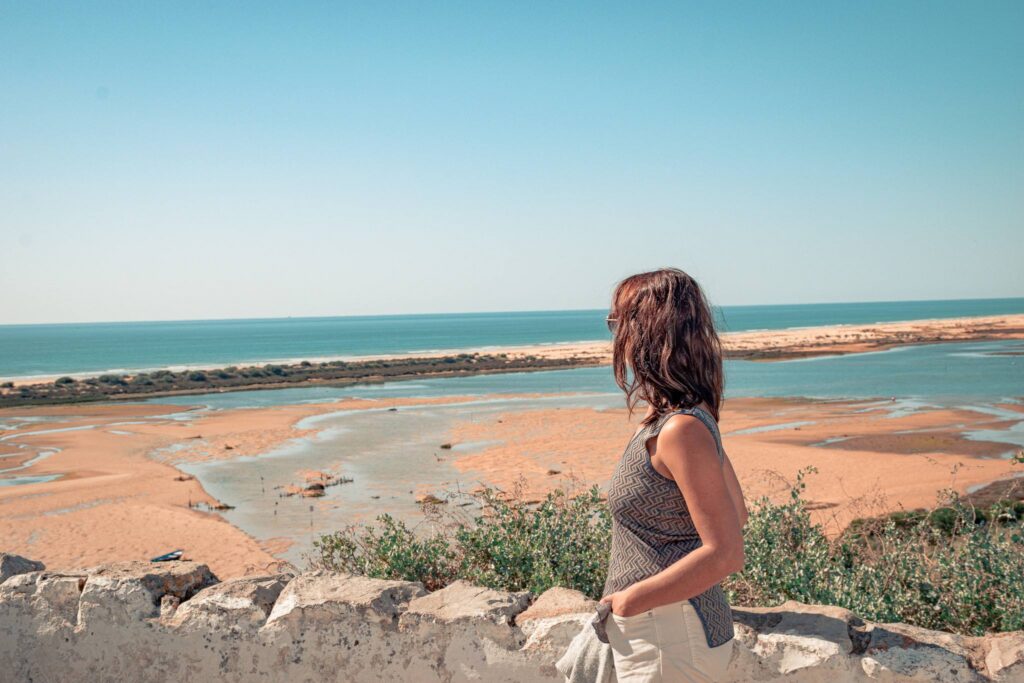 Caroline observes the lagoon and the beach of Cacela Velha from the cliff, with the Atlantic Ocean in the distance.