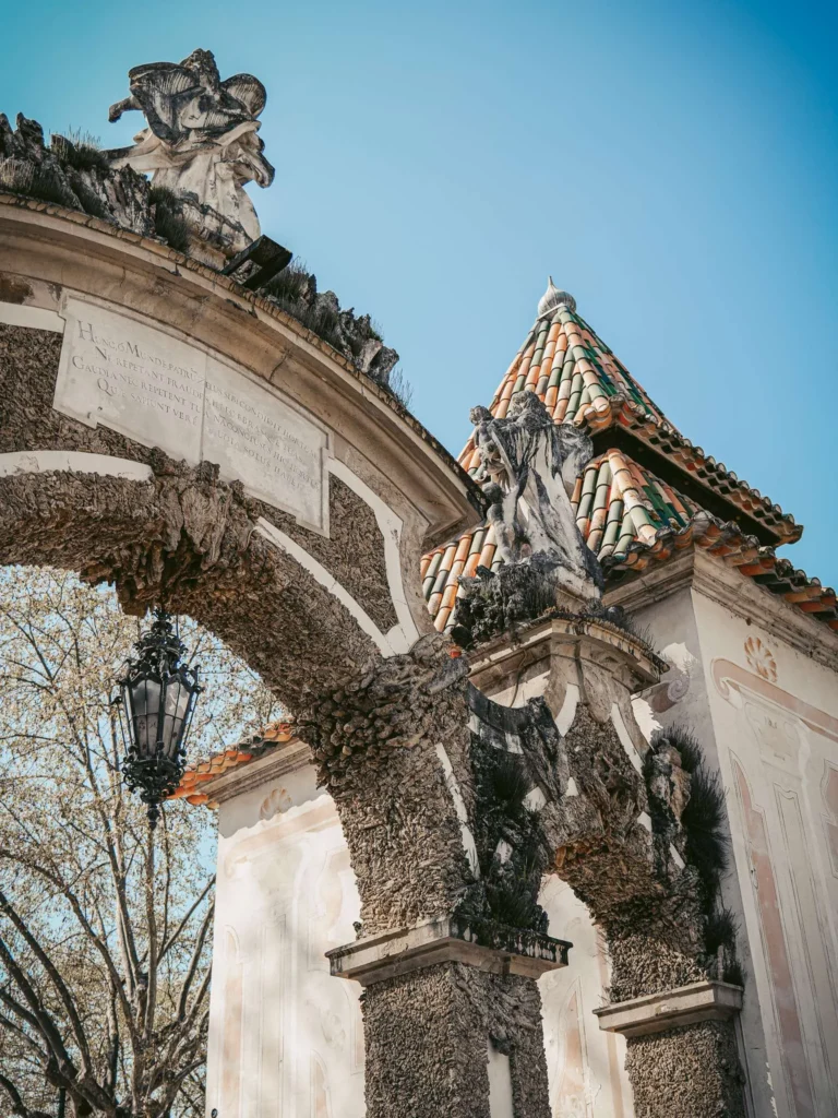 Ornamental gate of the Sereia garden in Coimbra, Portugal, featuring baroque sculptures and a colorful tiled roof under a blue sky in spring.