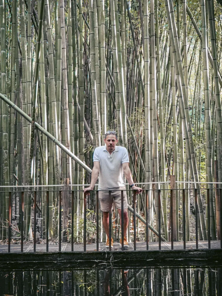 Xavier standing on a walkway in front of a bamboo forest at the Botanical Garden of Coimbra, spring atmosphere.