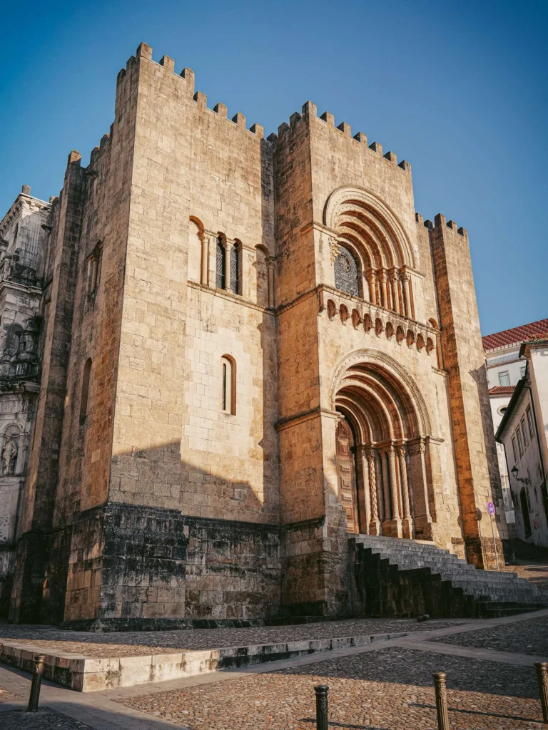 Main facade of the Sé Velha de Coimbra, an imposing Romanesque stone cathedral under a clear sky.