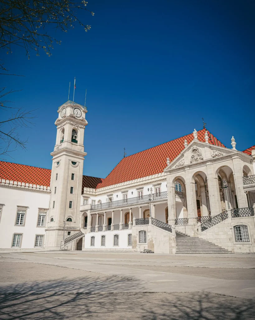 Historic building of the University of Coimbra under a blue sky, with its iconic tower and red tiled roofs.