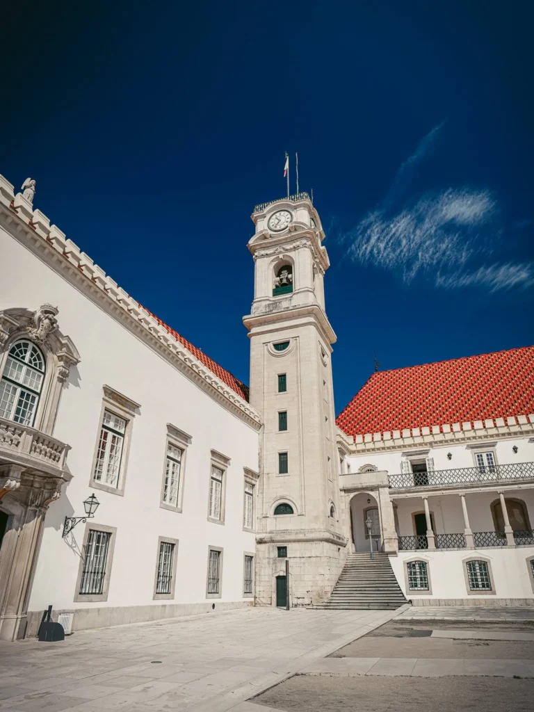 The main courtyard of the University of Coimbra with its famous clock tower under a blue sky, Portuguese historical architecture.