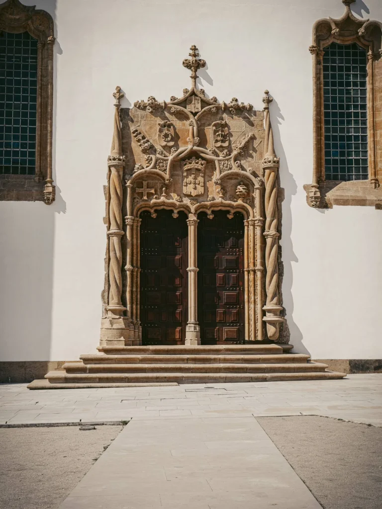 Portal adorned in Manueline style on the façade of a historic building in Coimbra, illuminated by daylight. No passerby visible in front of the monumental entrance.