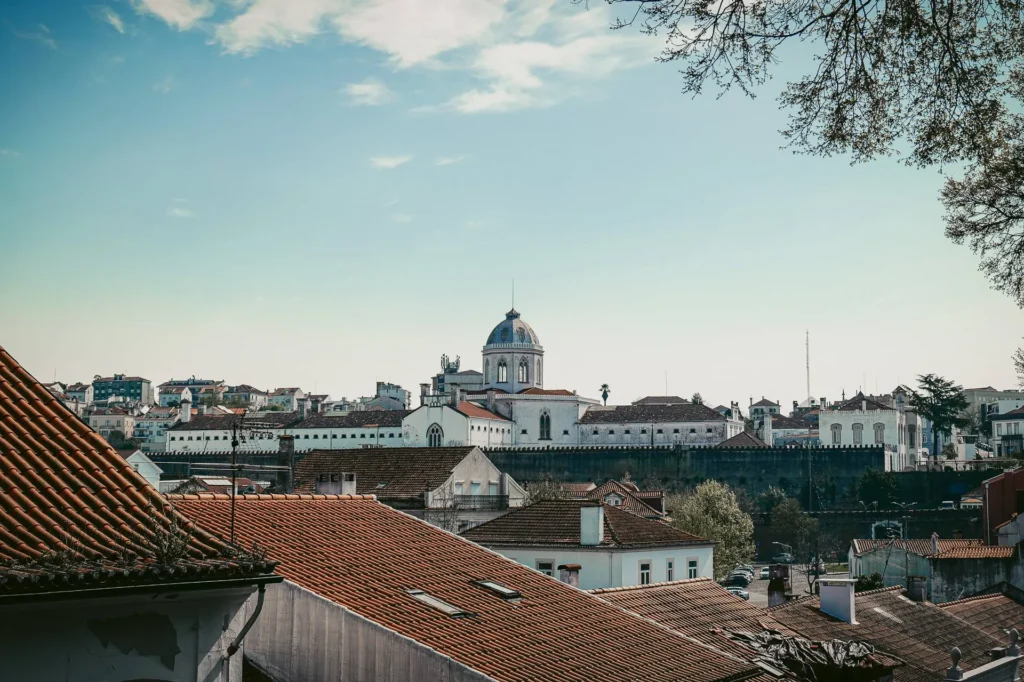 View of the rooftops of Coimbra with a historic dome building in the background under a partially cloudy sky, in Portugal at the end of March.