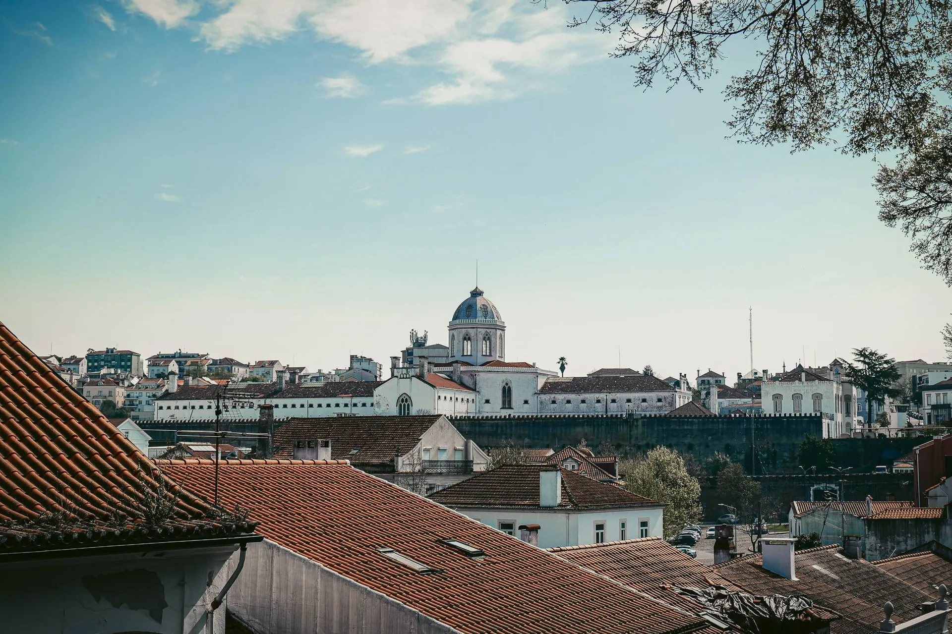 View of the rooftops of Coimbra with a historic dome building in the background under a partially cloudy sky, in Portugal at the end of March.