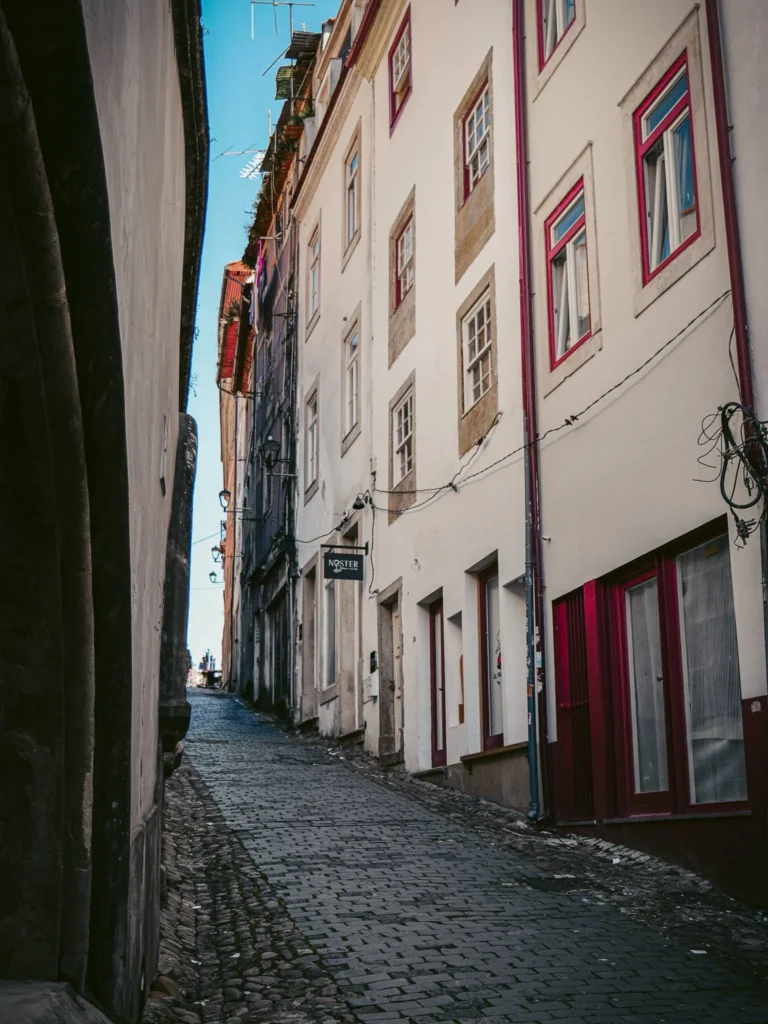 Paved sloping street lined with old buildings in Coimbra, Portugal, under a clear sky.