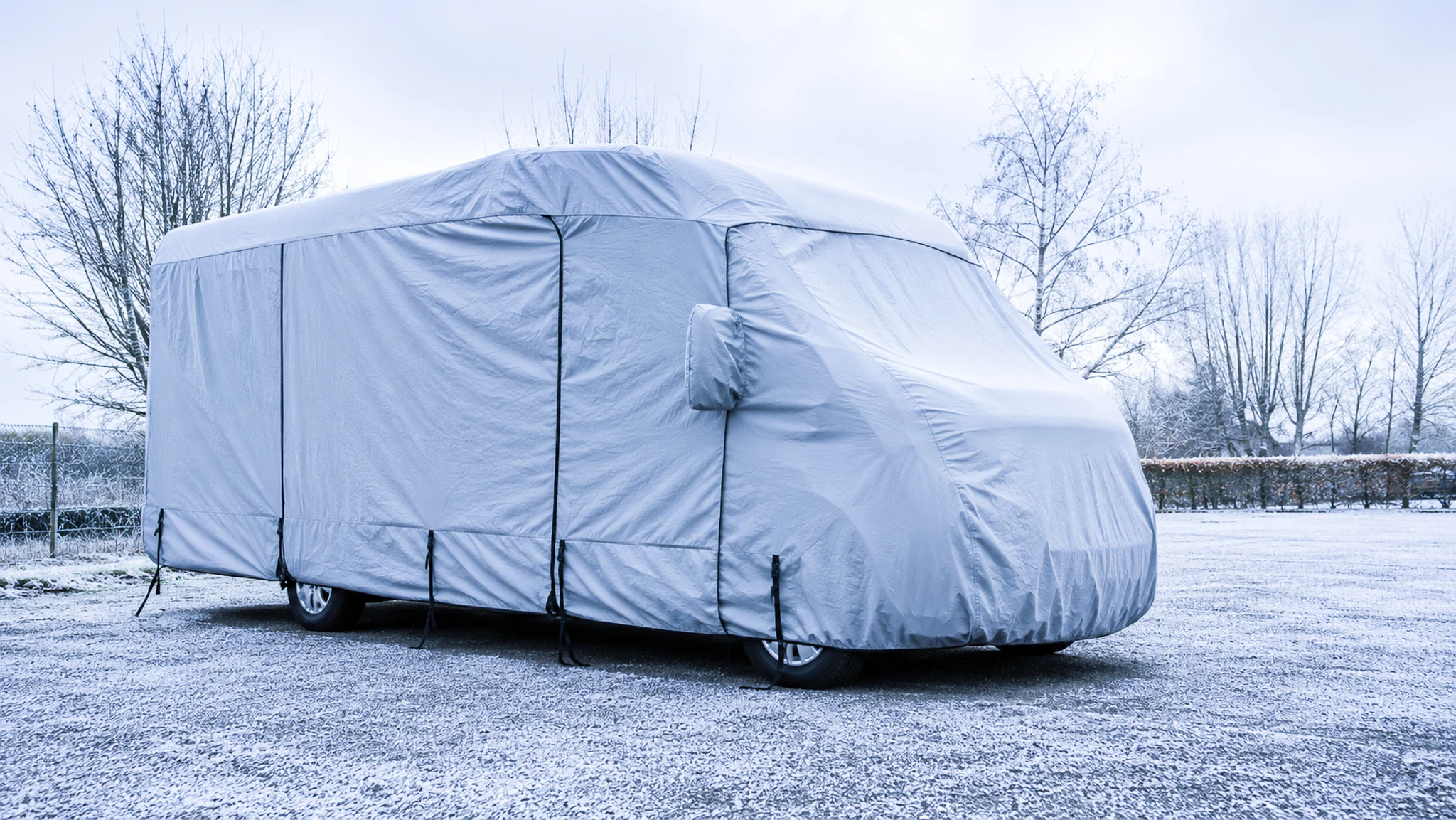 Motorhome covered with a protective cover in winter, parked in a snowy landscape