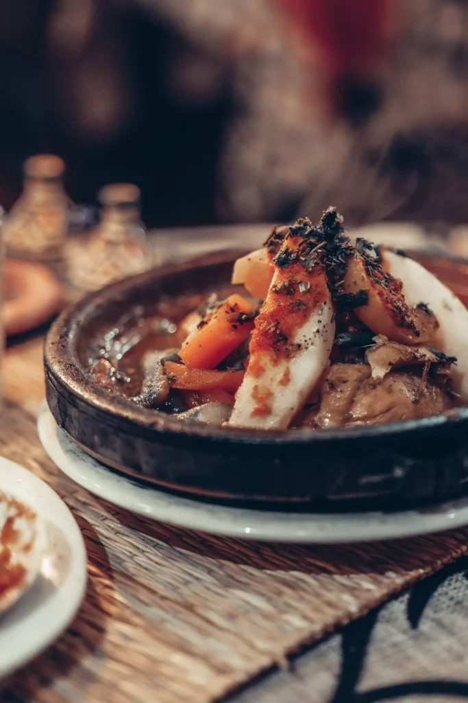 A chicken tagine with preserved lemons and vegetables served in a clay dish on a restaurant table in Essaouira.