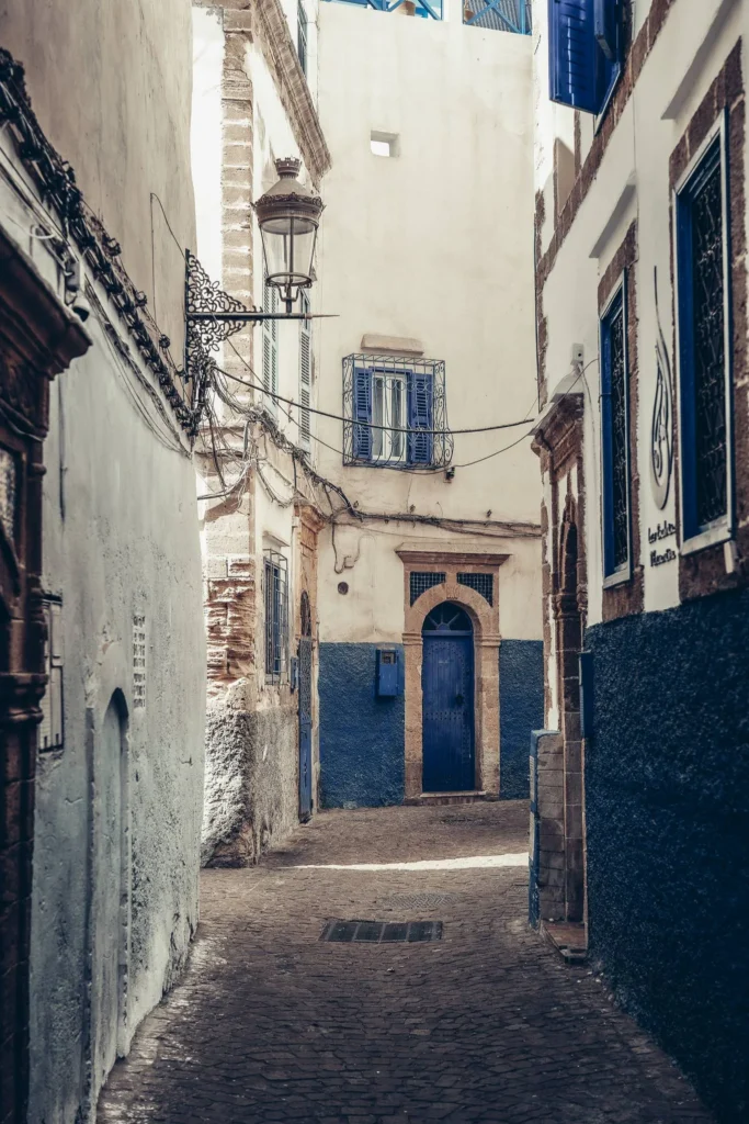 Narrow alley in the medina of Essaouira with white and blue walls, traditional shutters and doors, calm atmosphere during the day.