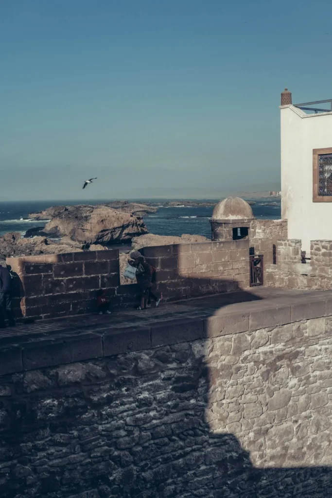 Stone ramparts overlooking the Atlantic Ocean in Essaouira, Morocco, under a clear sky with a view of the rocks and a seagull in flight.