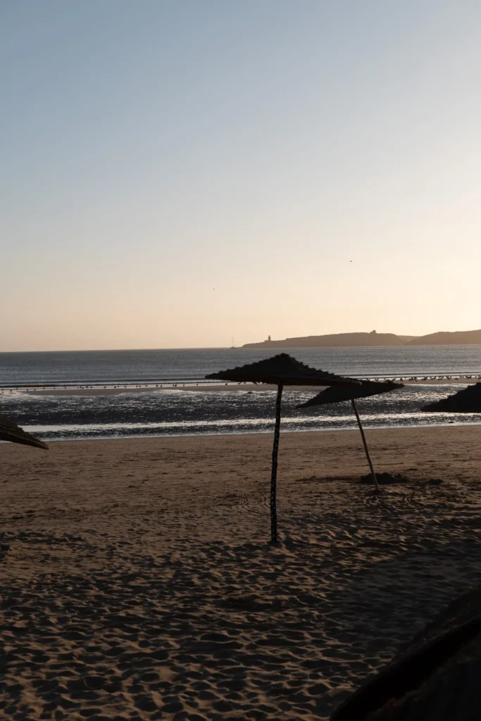 Sandy beach in Essaouira at sunset, straw umbrellas and a view of the Atlantic Ocean.