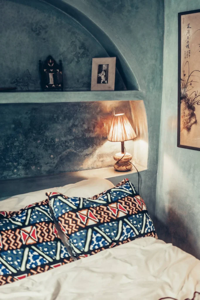 Room decorated in Moroccan style with colorful cushions, a bedside lamp, and tadelakt walls, at Riad El Rahala in Essaouira in October 2025.