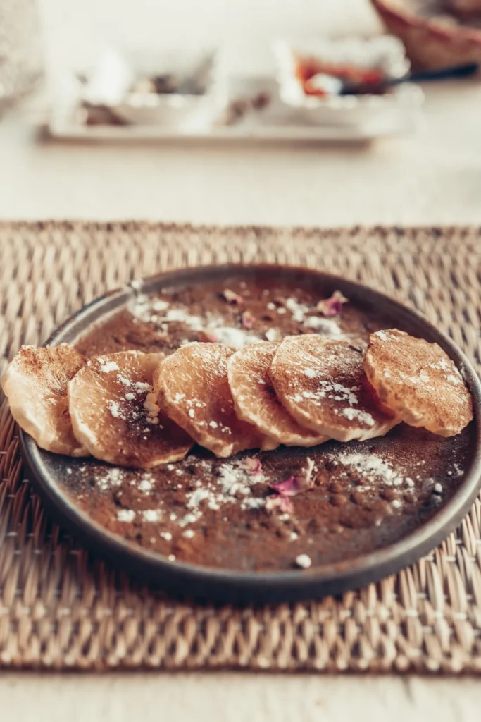 Orange-based dessert, sprinkled with cinnamon and sugar, served on a ceramic plate in a warm atmosphere in Essaouira, Morocco.