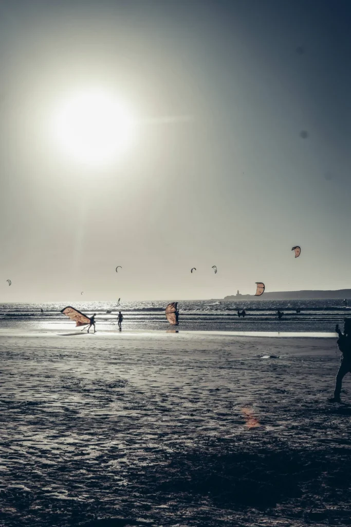 Essaouira beach in Morocco at the end of the day, several people are kitesurfing under a bright sun.