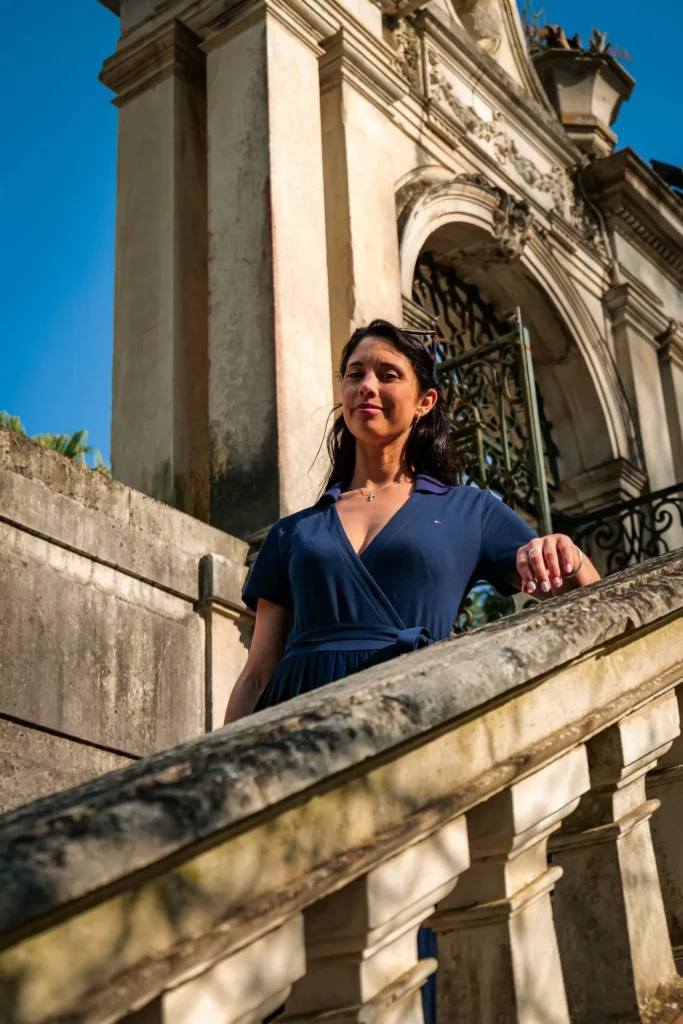 Caroline poses on a stone staircase in front of a monumental entrance to the Botanical Garden of Coimbra, under a spring light.