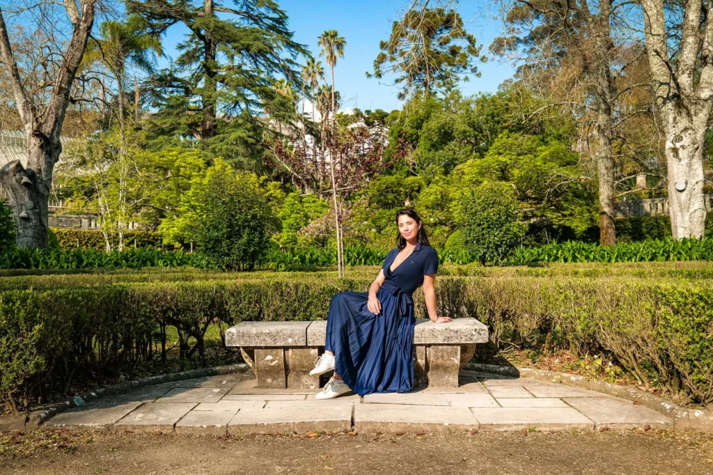 Caroline sitting on a stone bench in the Botanical Garden of Coimbra, surrounded by greenery at the beginning of spring.