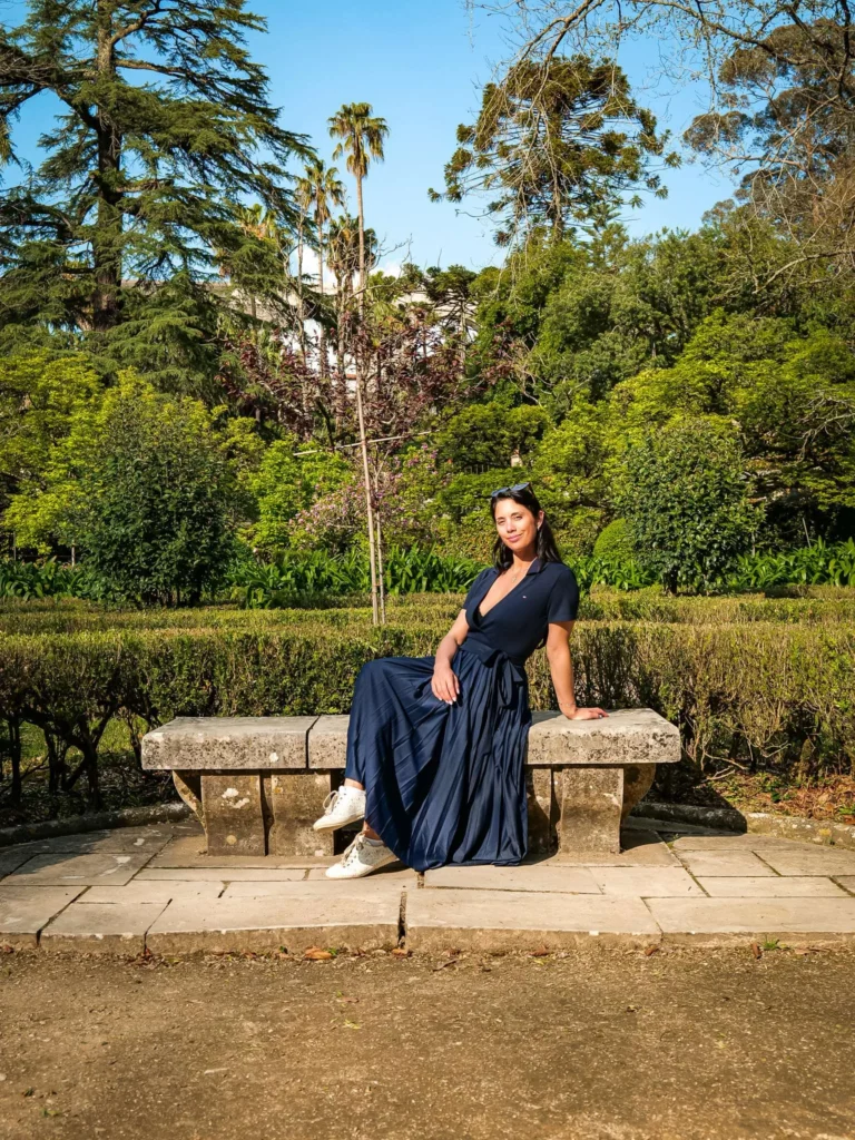 Caroline sitting on a stone bench in the Botanical Garden of Coimbra, surrounded by lush vegetation on a sunny spring day.