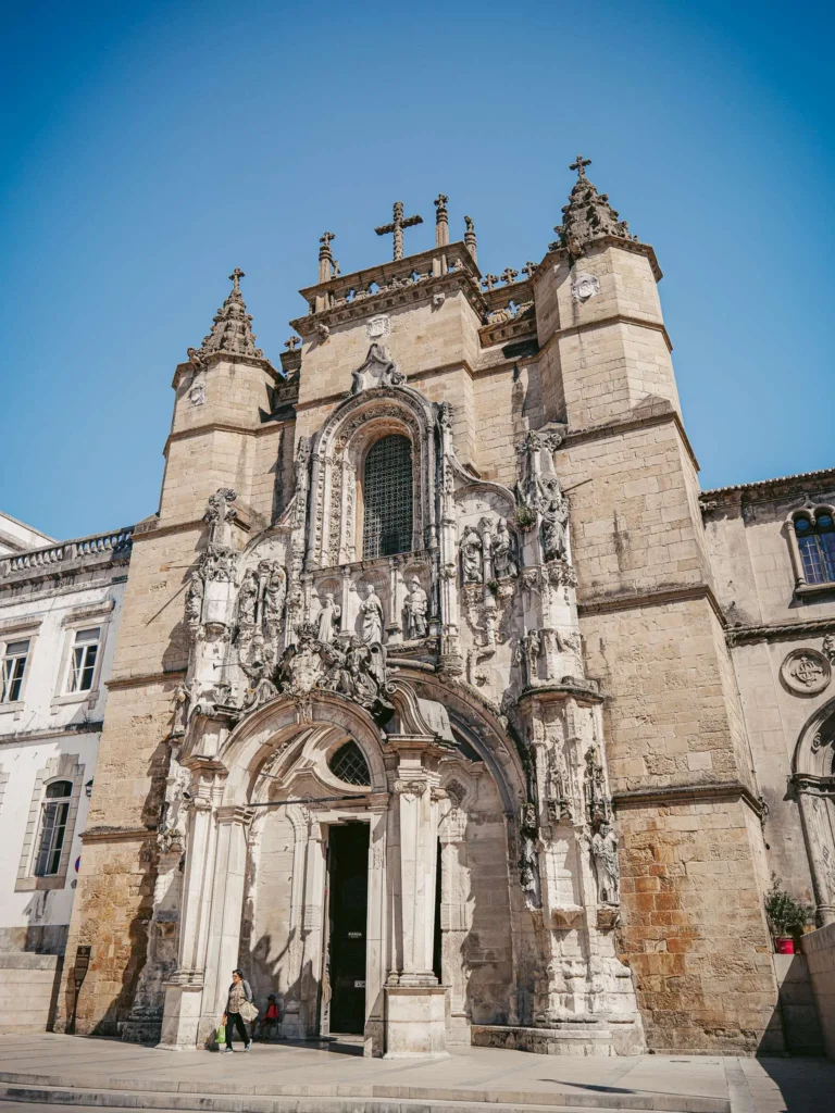 Facade of the Santa Cruz church in Coimbra, Gothic-Manueline architecture under a clear sky, no identifiable visitors in the foreground.