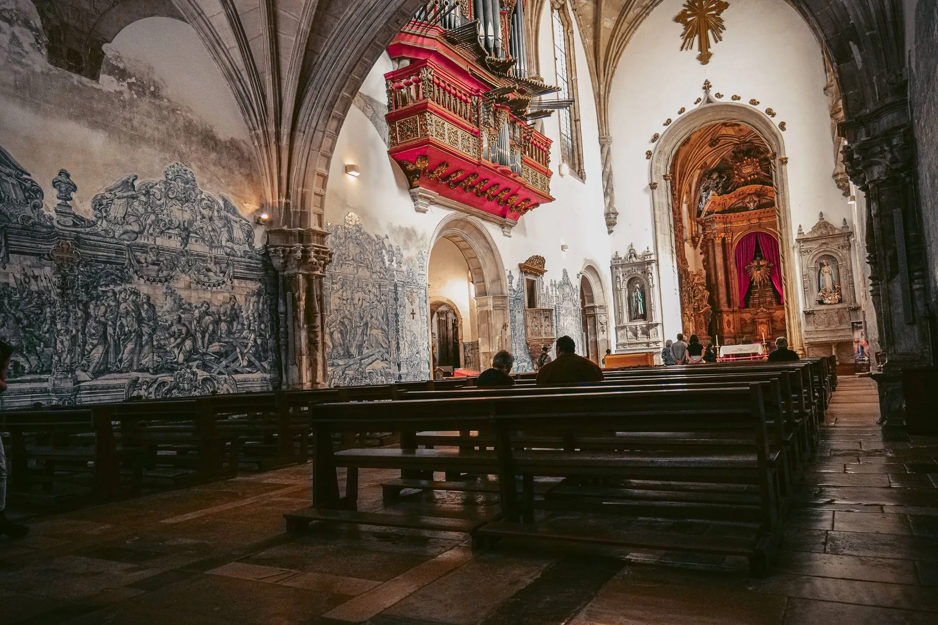 Interior of the Santa Cruz church in Coimbra, with its blue azulejos, a suspended red baroque organ, and wooden benches, photographed on March 29, 2026.