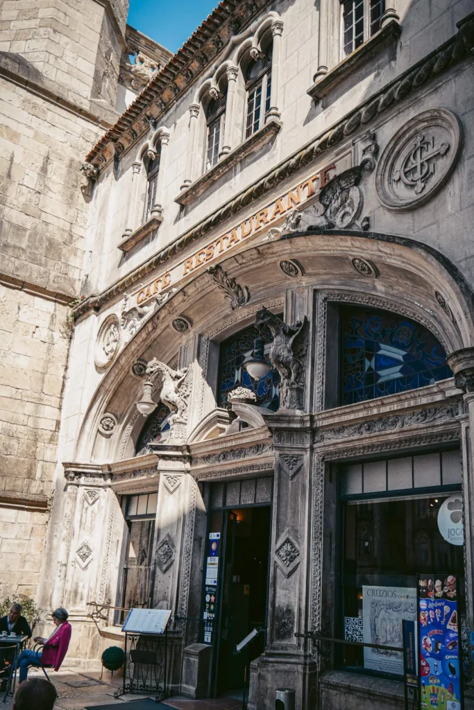 Historical facade of an ornate architecture café-restaurant located on a sunny street in Coimbra, Portugal, with a few people sitting on the terrace.