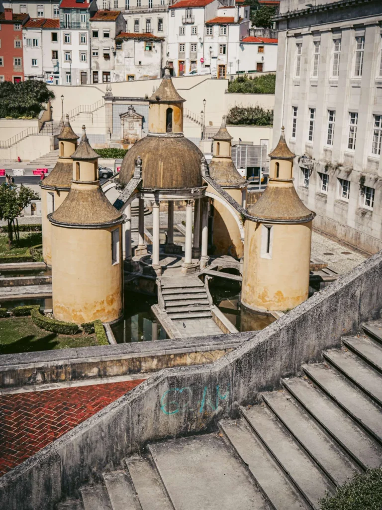 Monumental fountain of Jardim da Manga in Coimbra, surrounded by stone stairs and historic buildings under a sunny sky.