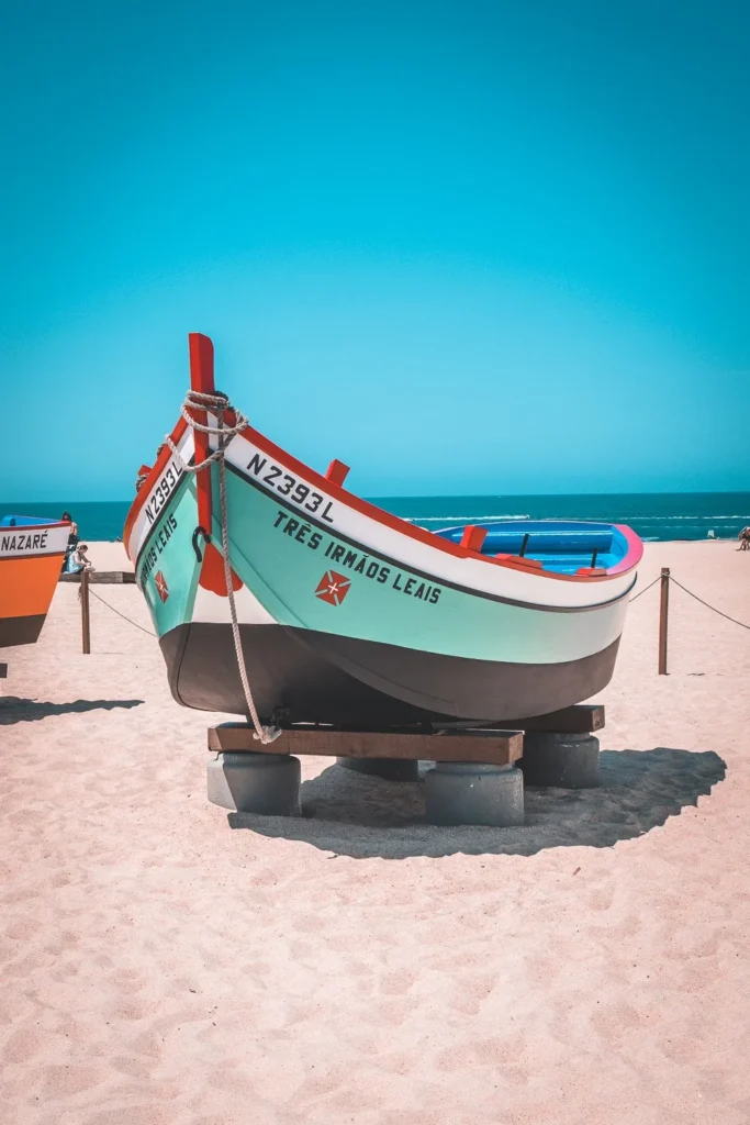 Colorful traditional fishing boat resting on the sand in Nazaré, under a blue sky in summer.